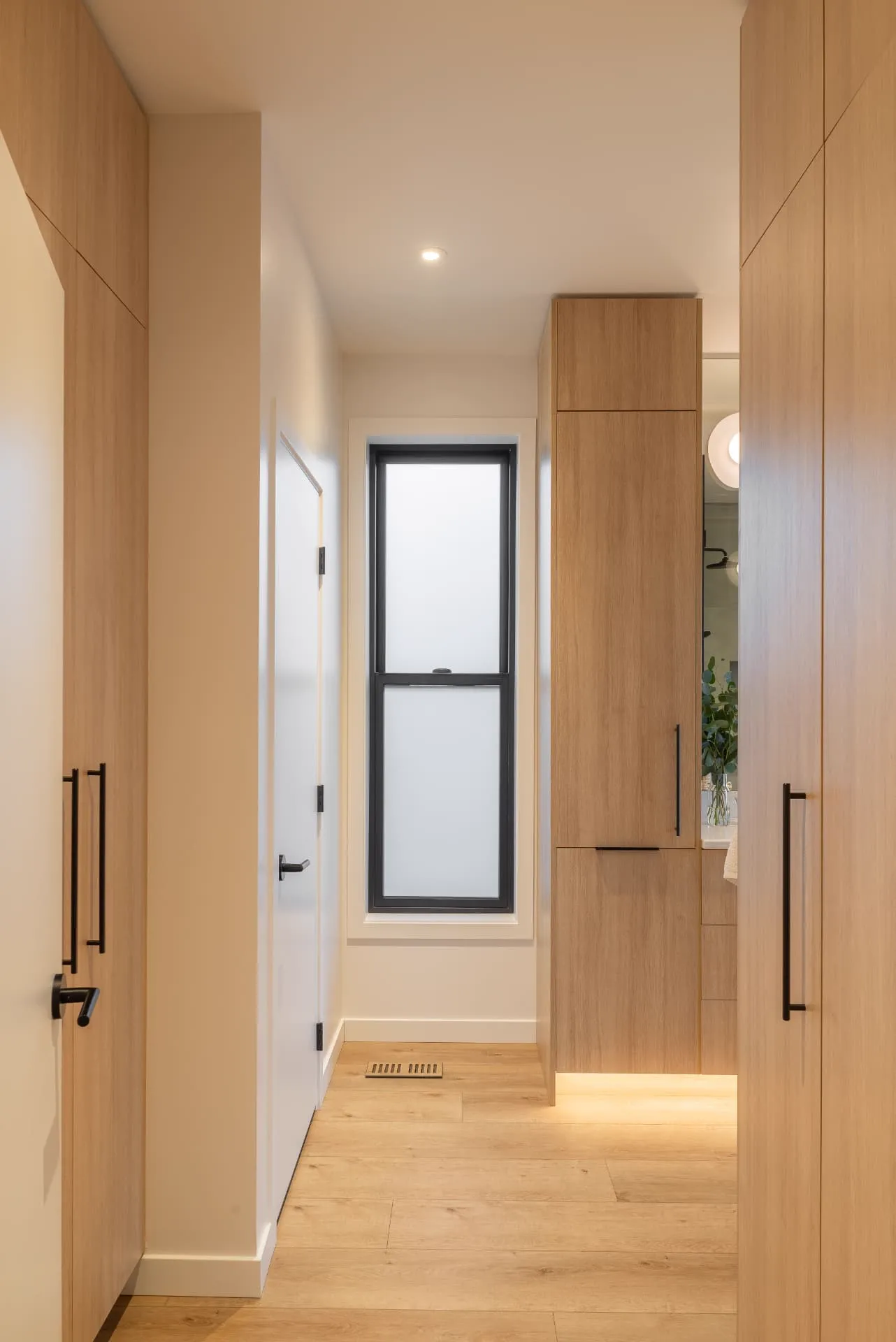 Abbott hallway, Penticton BC: white oak built-in cabinetry with black hardware, a tall black-framed frosted window, and light oak flooring