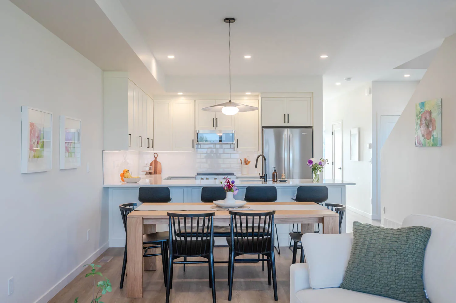Edgeview townhome kitchen and dining area, Penticton BC: white shaker cabinetry, quartz island seating, oak dining table, and black spindle chairs