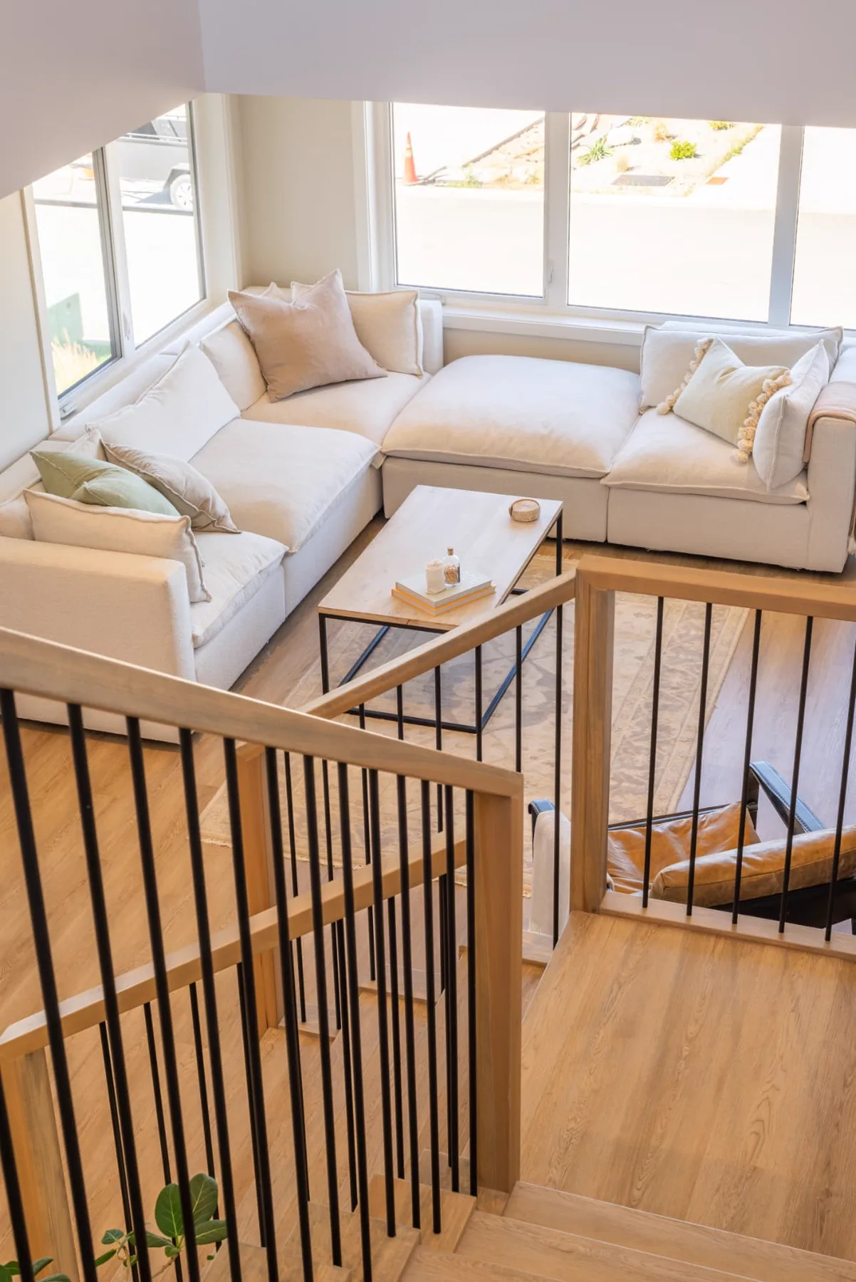 Ridge living room, Penticton BC: cream sectional sofa and oak coffee table below wide windows, viewed over a white oak and black steel stair railing