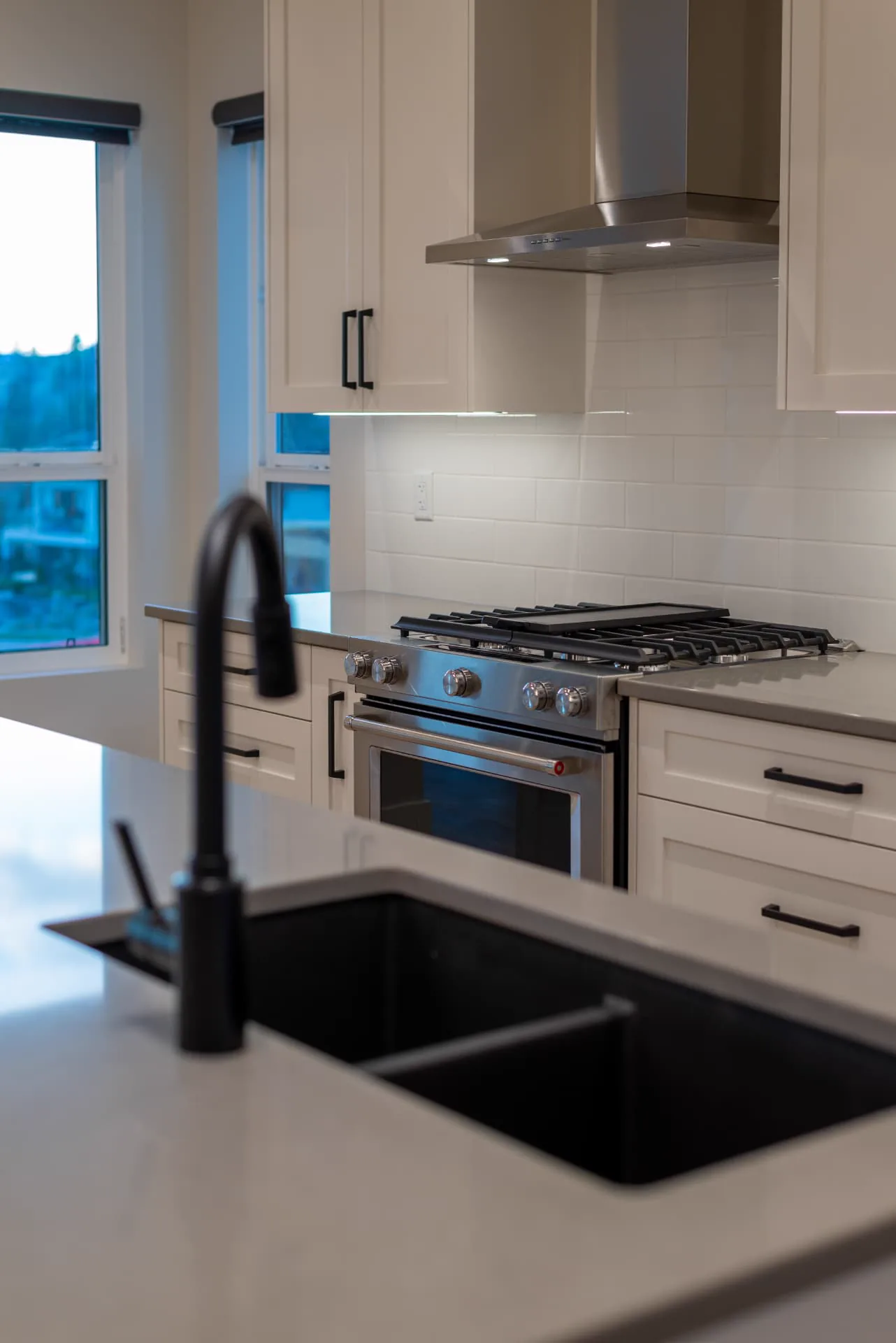 Fawn Court kitchen detail, Penticton BC: white cabinetry, stainless steel range, quartz counters, and a black sink and faucet