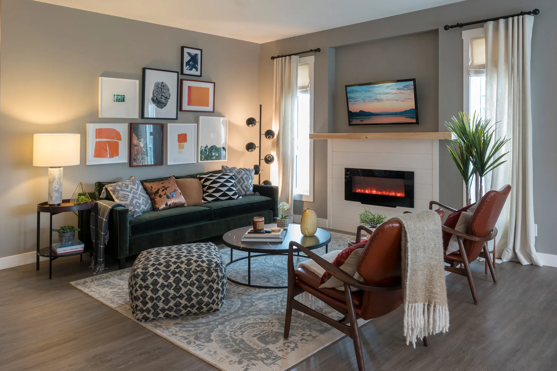 The Bow living room, Penticton BC: emerald velvet sofa, leather accent chairs, electric fireplace with shiplap surround, and curated gallery wall