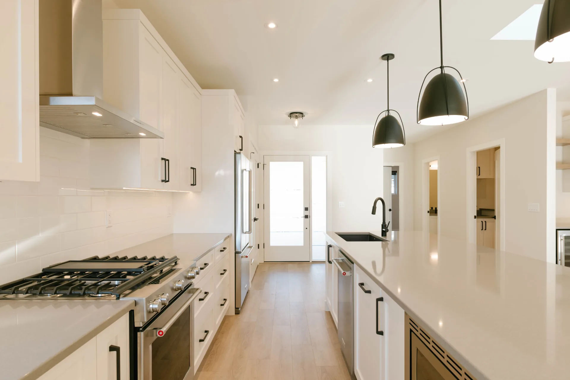 Fawn Court kitchen, Penticton BC: long quartz island, white cabinetry, black pendant lights, and light oak flooring