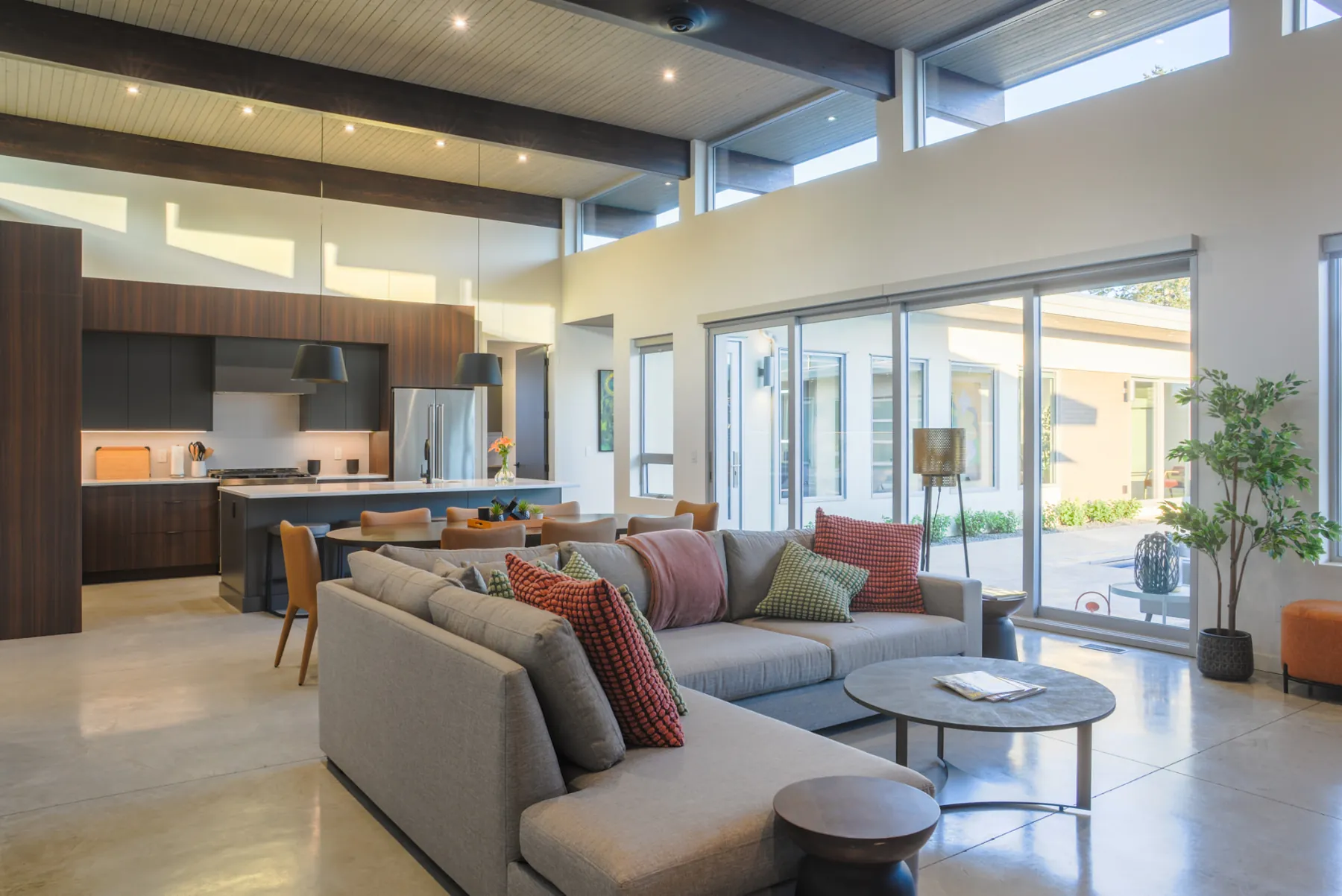 Ridgedale open-plan living and kitchen, Penticton BC: vaulted wood-beam ceiling, clerestory windows, walnut cabinetry, and sliding doors onto the courtyard