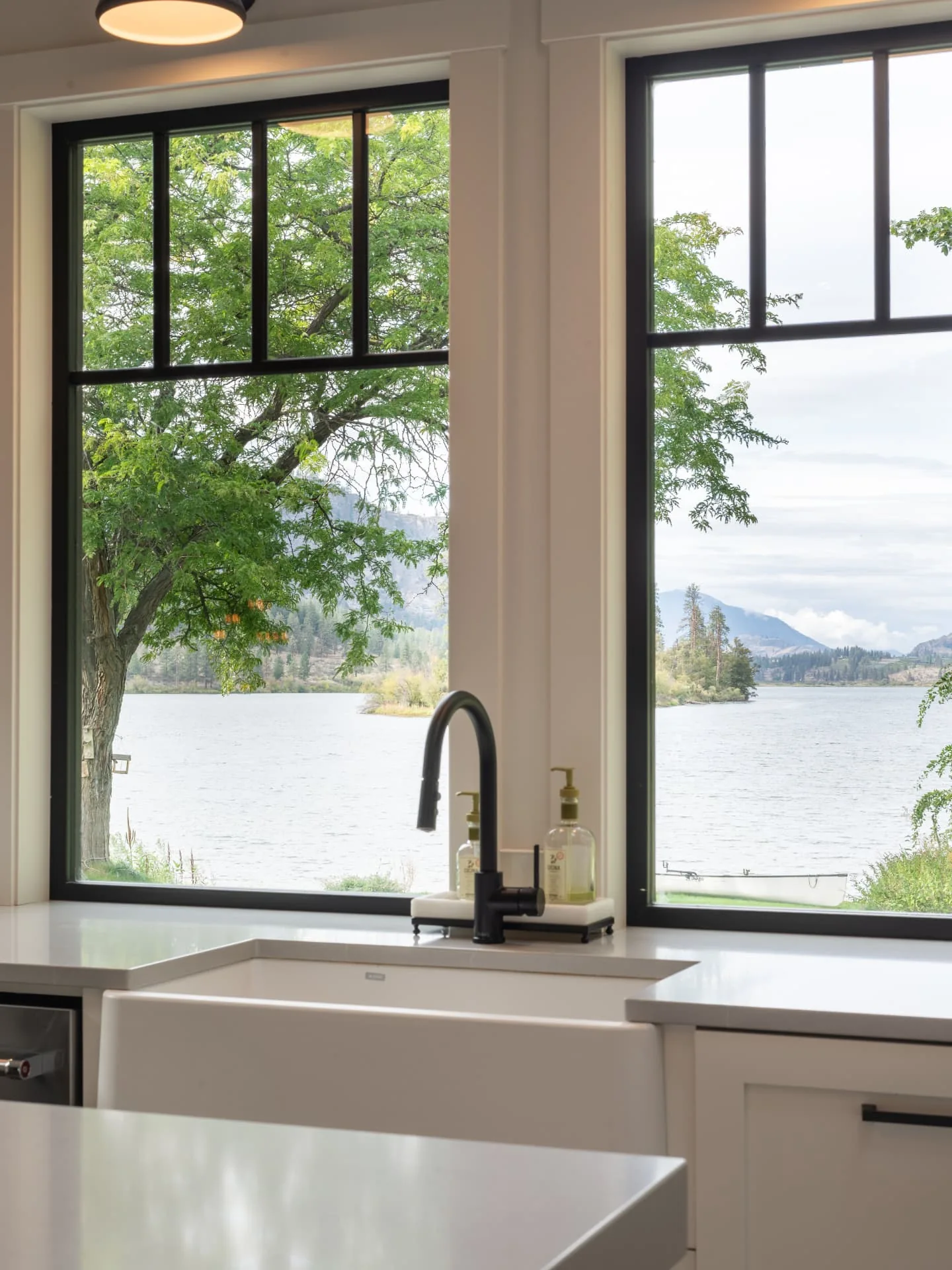 Sundial kitchen in Oliver, BC: farmhouse sink beneath tall black framed windows overlooking the lake