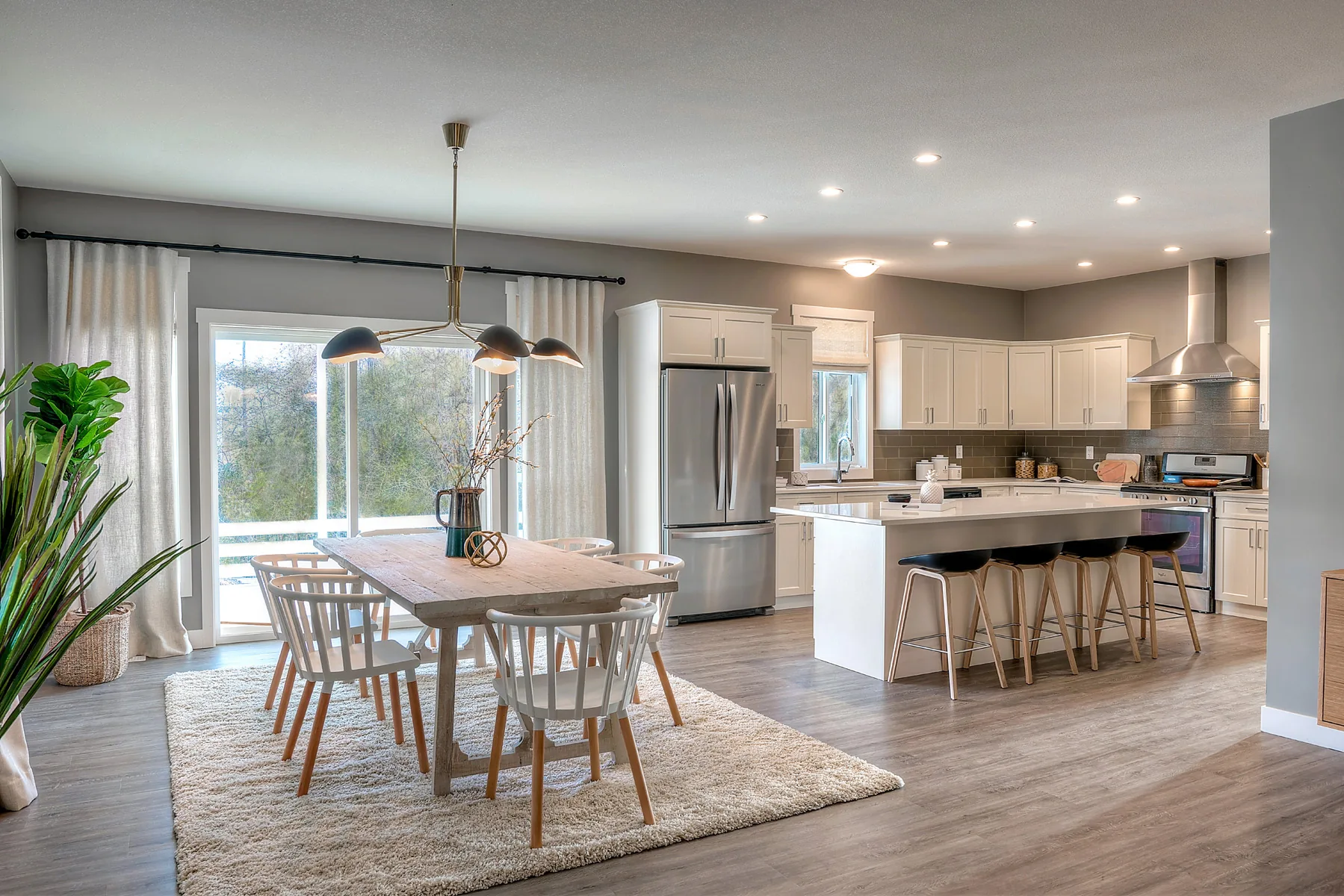 The Bow kitchen and dining area, Penticton BC: white shaker cabinetry, quartz waterfall island with black bar stools, oak dining table, and sliding glass doors to the patio