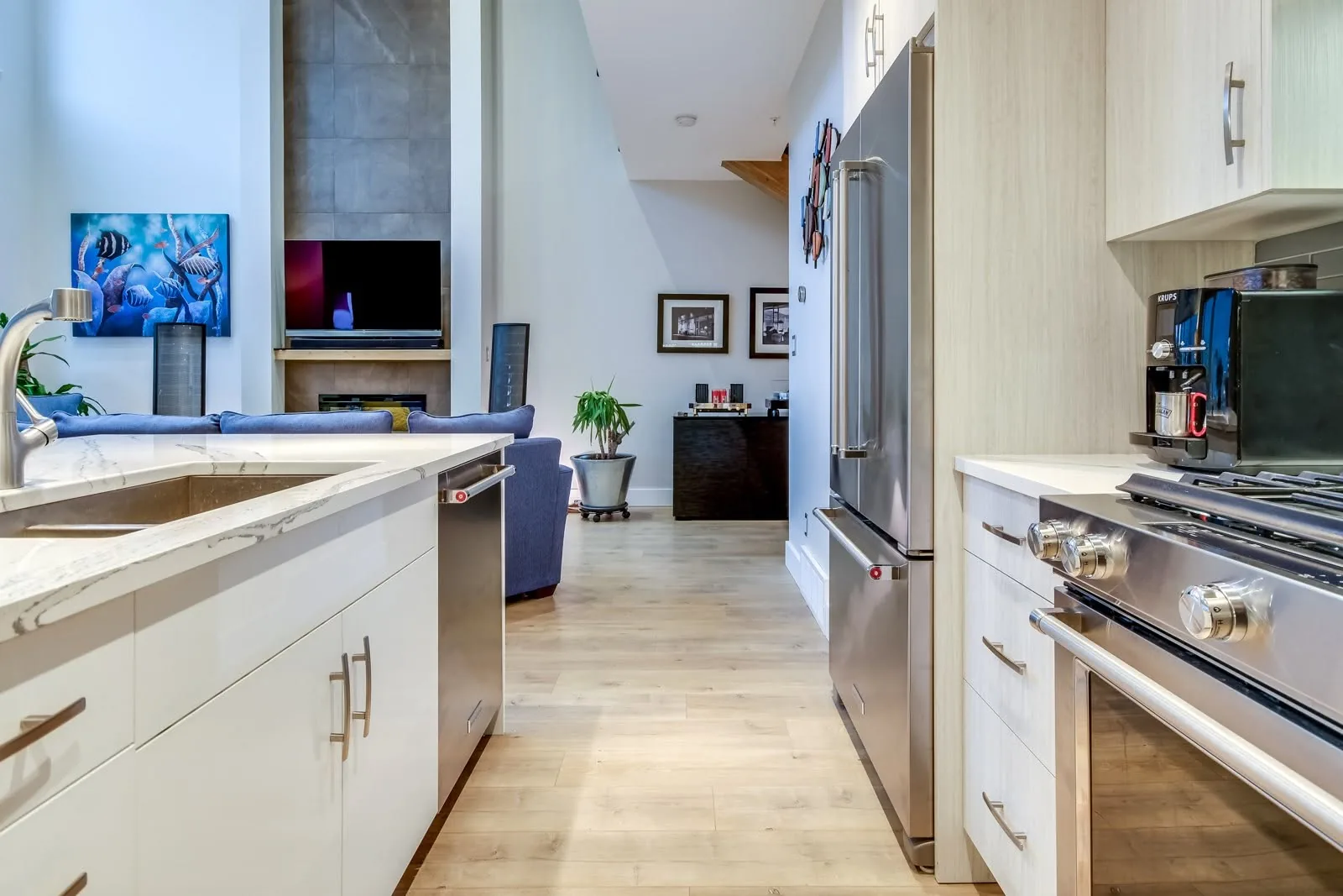 Beechwood interior, Penticton BC: modern kitchen with white cabinetry, stainless appliances, and a view toward a bright living room with a fireplace and tall ceilings