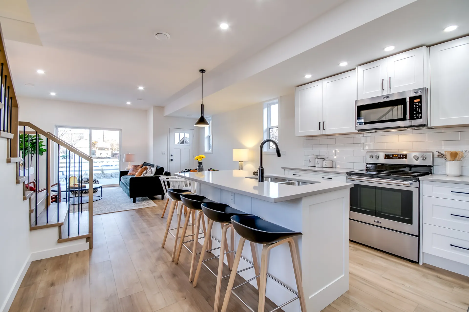 Douglas Ave open-concept kitchen and living room, Penticton BC: white shaker cabinetry, quartz waterfall island with black bar stools, and a bright living area beyond