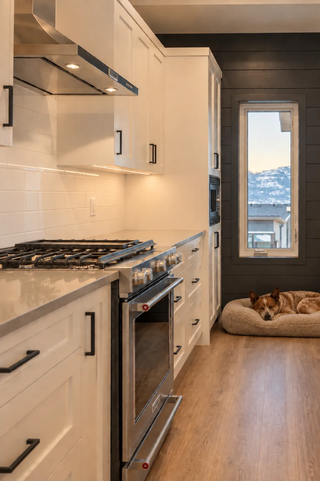 Fawn Court II kitchen, Penticton BC: white shaker cabinetry with a black shiplap accent wall, stainless range with a vented hood, subway tile backsplash, and a tall window framing Okanagan mountain views