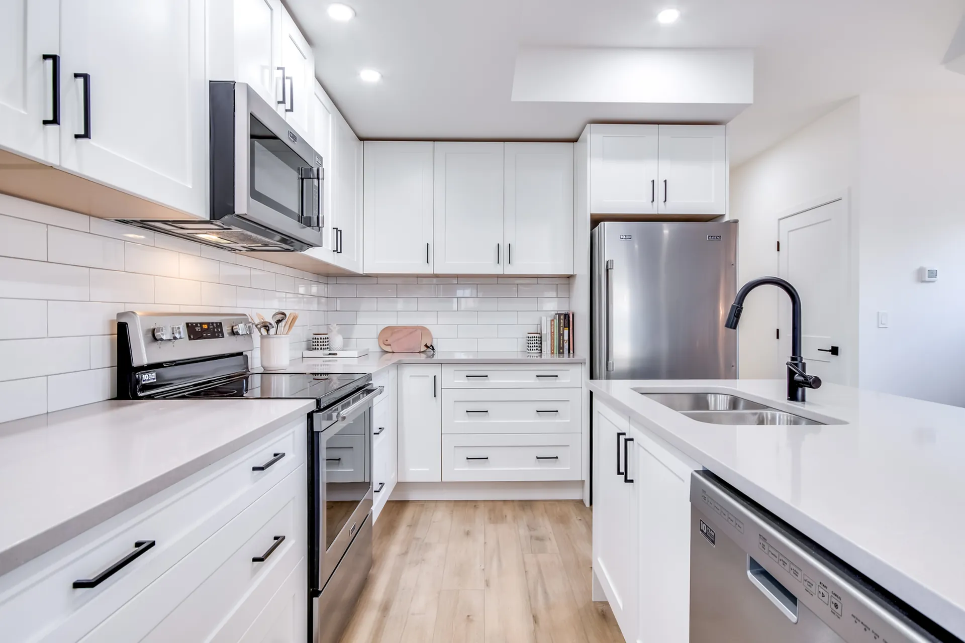 Douglas Ave galley kitchen, Penticton BC: white cabinetry with black hardware, subway tile backsplash, stainless appliances, and quartz counters