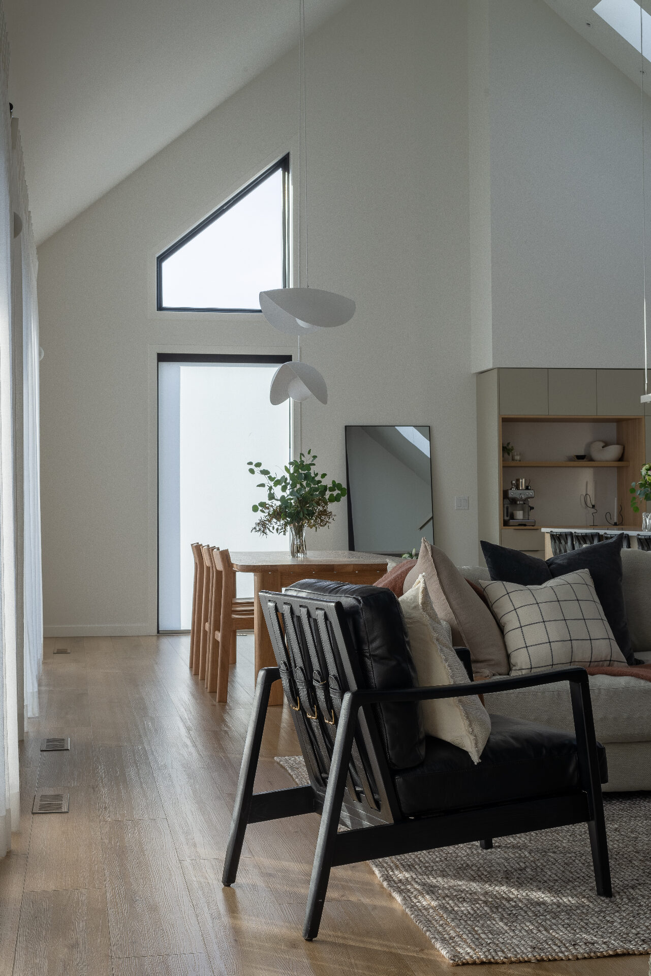 Light-filled living and dining area with vaulted ceiling, oak floors, and a black-framed window opening to the South Okanagan.