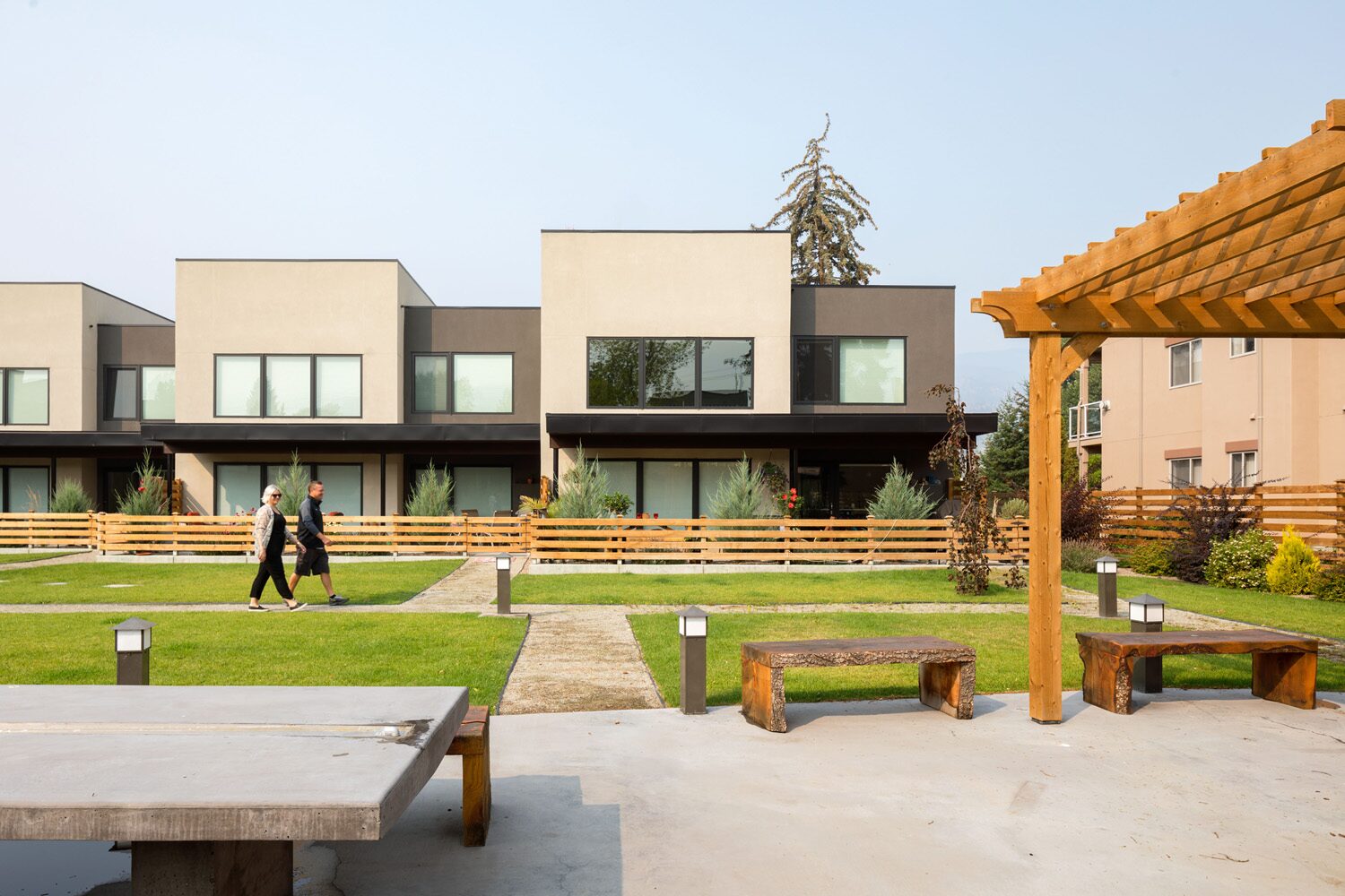 Beechwood Urban Collection courtyard in Penticton, BC: modern stucco townhomes with cedar fencing, pergola, and shared green space between residents walking the path