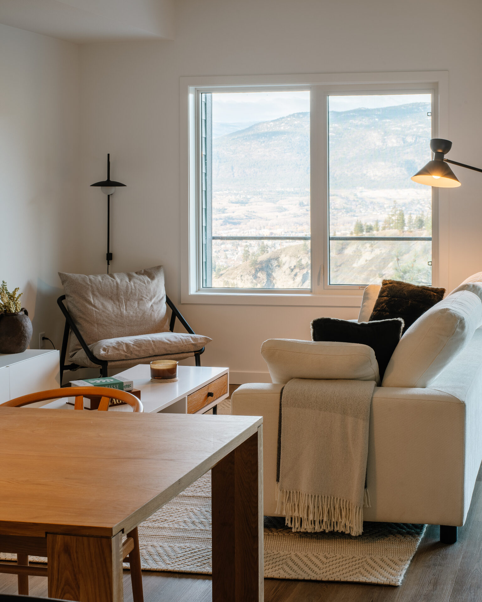 Urban Collection living and dining area with a linen sofa, oak dining table, and a large picture window framing a sweeping South Okanagan mountain and valley view.
